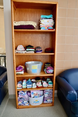A display of free donated baby items — including handmade hats, blankets, and other gifts — offers comfort and warmth to new parents at Naval Hospital Twentynine Palms. The display, located near the Multi-Service Ward, reflects the community’s support for military families and was featured as part of the ward’s revitalization, officially marked during a ribbon-cutting ceremony on May 29 (U.S. Navy photo by Christopher C. Jones, NHTP/NMRTC Twentynine Palms public affairs officer).
