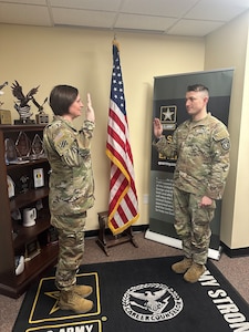 Two Soldiers standing in an office with a flag in the background.