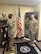 Two Soldiers standing in an office with a flag in the background.
