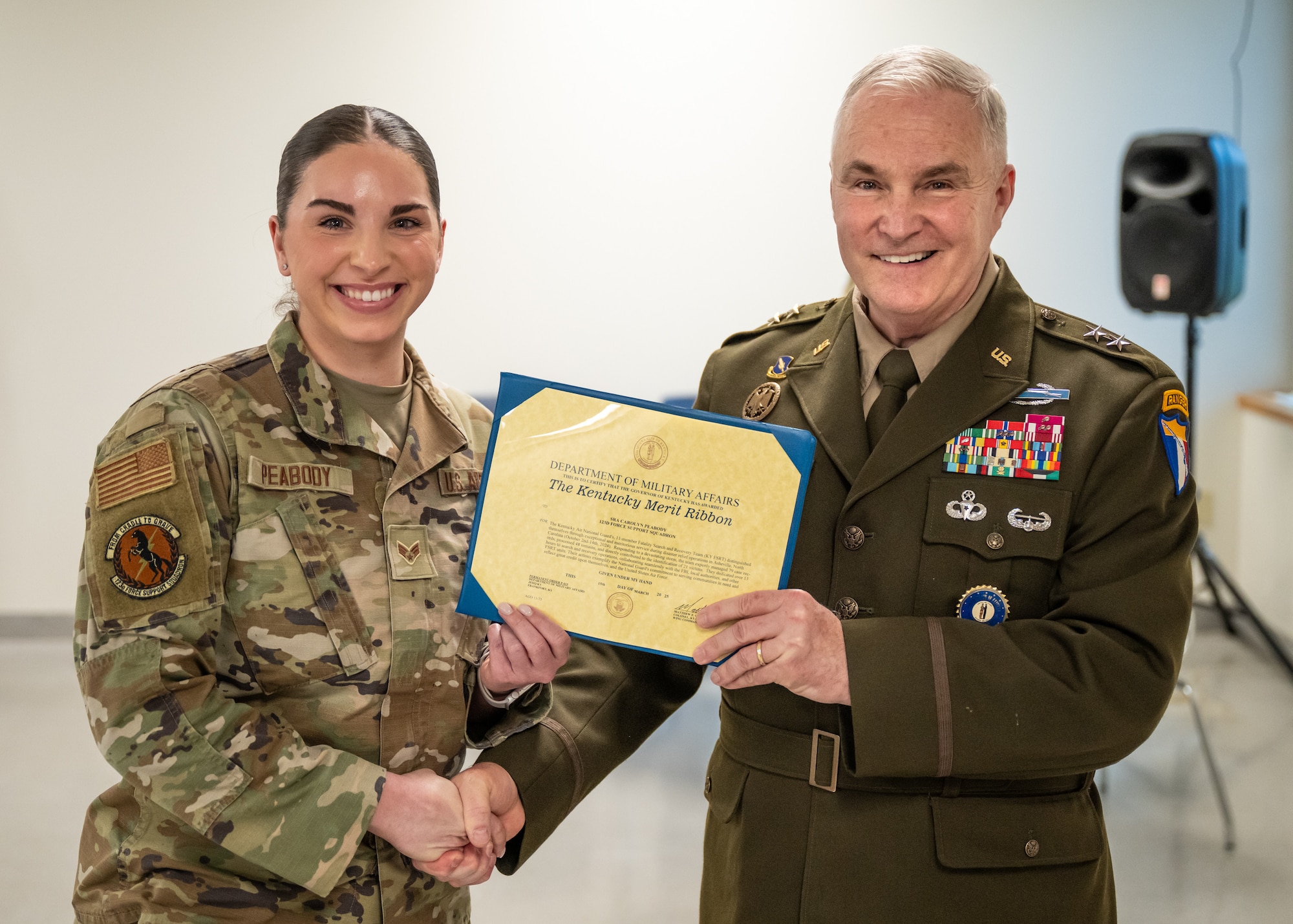Senior Airman Carolyn Peabody, left, is one of 11 members of the 123rd Airlift Wing Fatality Search and Recovery Team who was recognized with two decorations during a ceremony at the Kentucky Air National Guard Base in Louisville, Ky., April 13, 2025, for disaster-recovery work following Hurricane Helene in North Carolina. The Airmen each received a Kentucky National Guard Merit Ribbon and a North Carolina National Guard State Active Duty Ribbon from U.S. Army Maj. Gen. Haldane Lamberton, Kentucky's adjutant general, for exceptional and meritorious service from Oct. 2 to 14, 2024, in Asheville, N.C., where they managed the case records of 79 victims, processed 48 remains, directly contributed to the identification of 21 deceased and dedicated more than 13 hours to search and recovery operations, collaborating seamlessly with the FBI, local authorities and other FSRT units. (U.S. Air National Guard photo by Dale Greer)