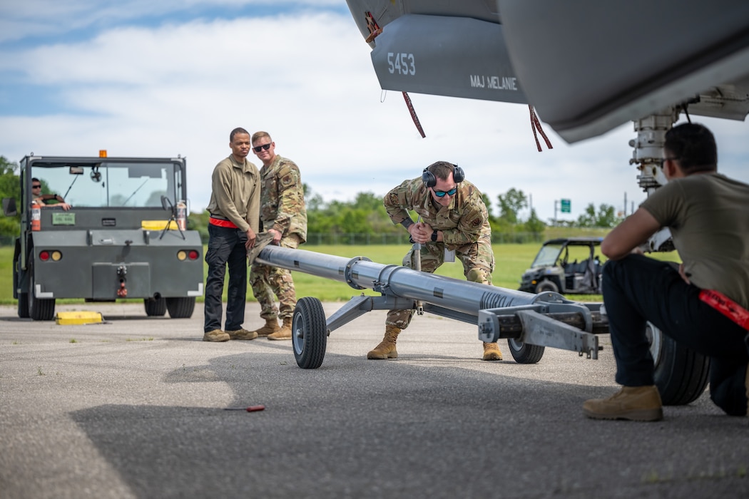 Service members guide a tow hitch on wheels to the front wheel of an aircraft