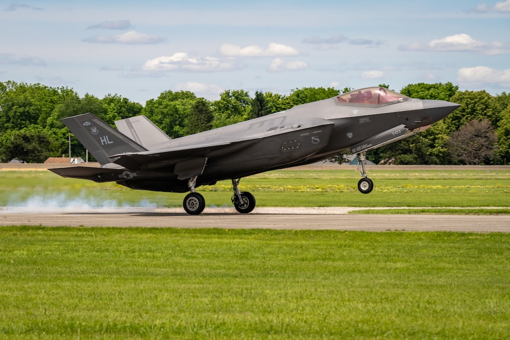 An F-35 lands on a runway, smoke coming from the rear wheels
