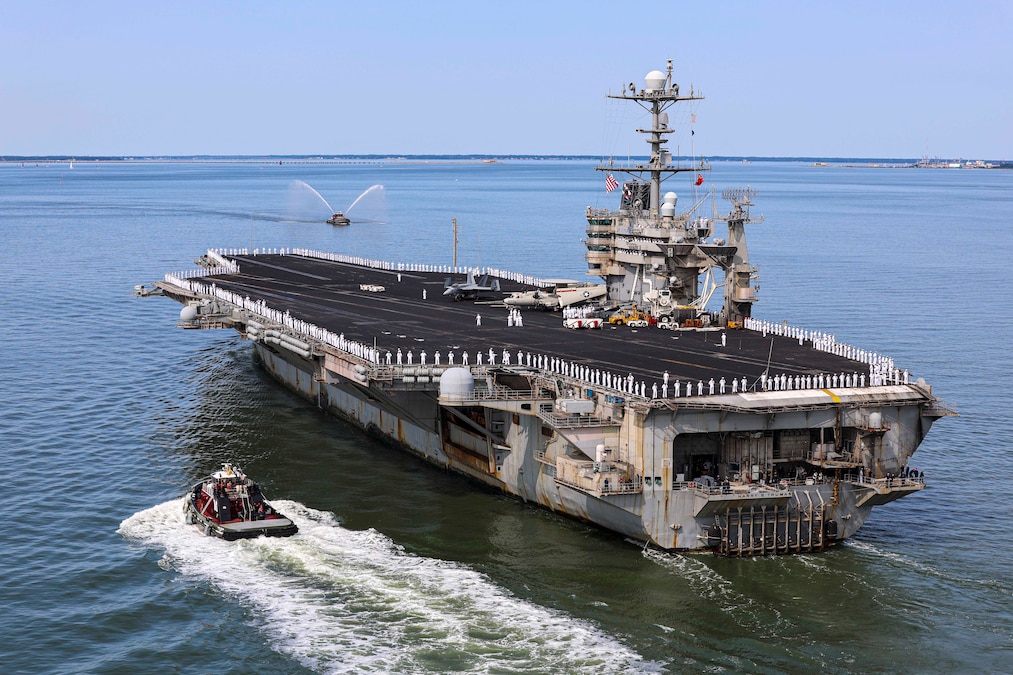 An aircraft carrier ship sails on the ocean with a small boat beside it.
