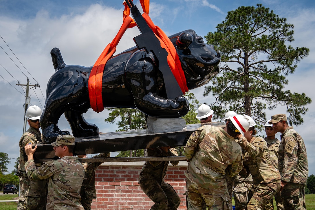 A group of soldiers hold up a large statue of a bulldog outside.