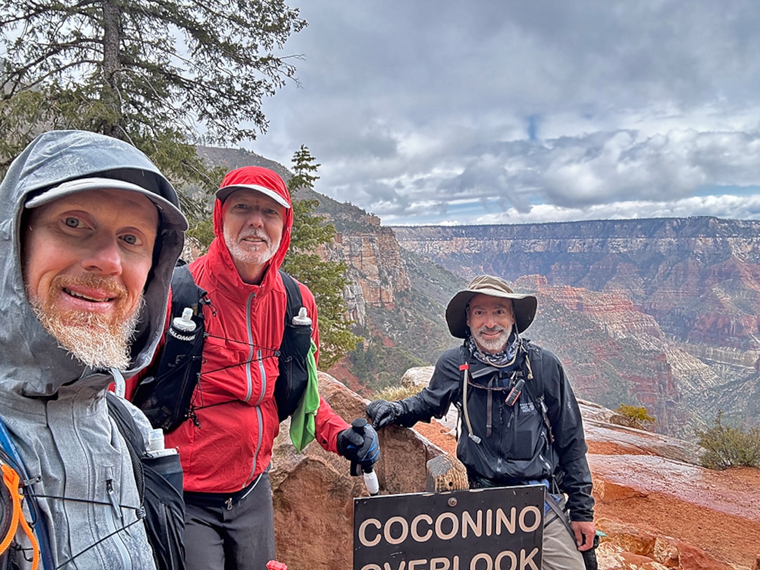 Three hikers pose for a photo near the rim of the Grand Canyon.