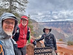 Three hikers pose for a photo near the rim of the Grand Canyon.
