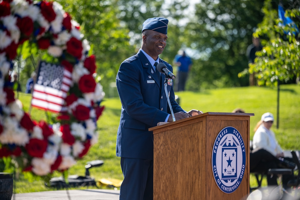 Col. Starks, wearing blue service dress uniform, stands behind a podium and microphone