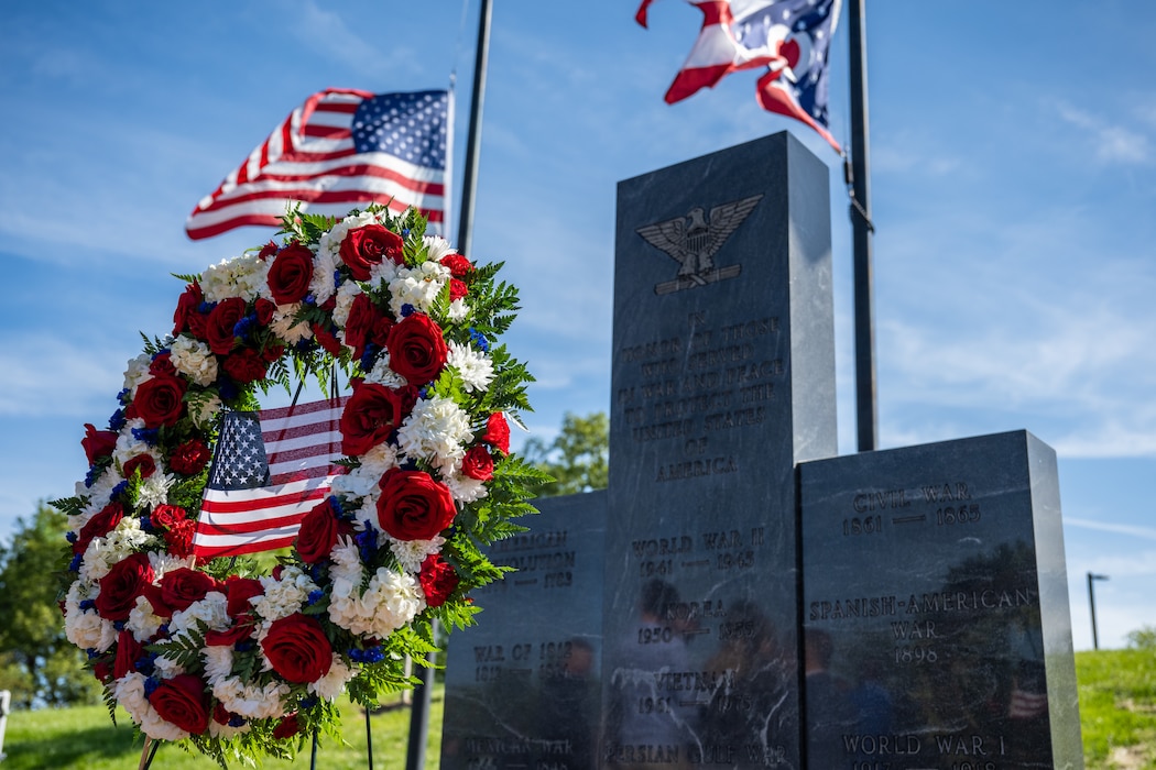 A wreath of flowers with a U.S. flag in the center, stands in front of three polished stone pillars in honor of veterans