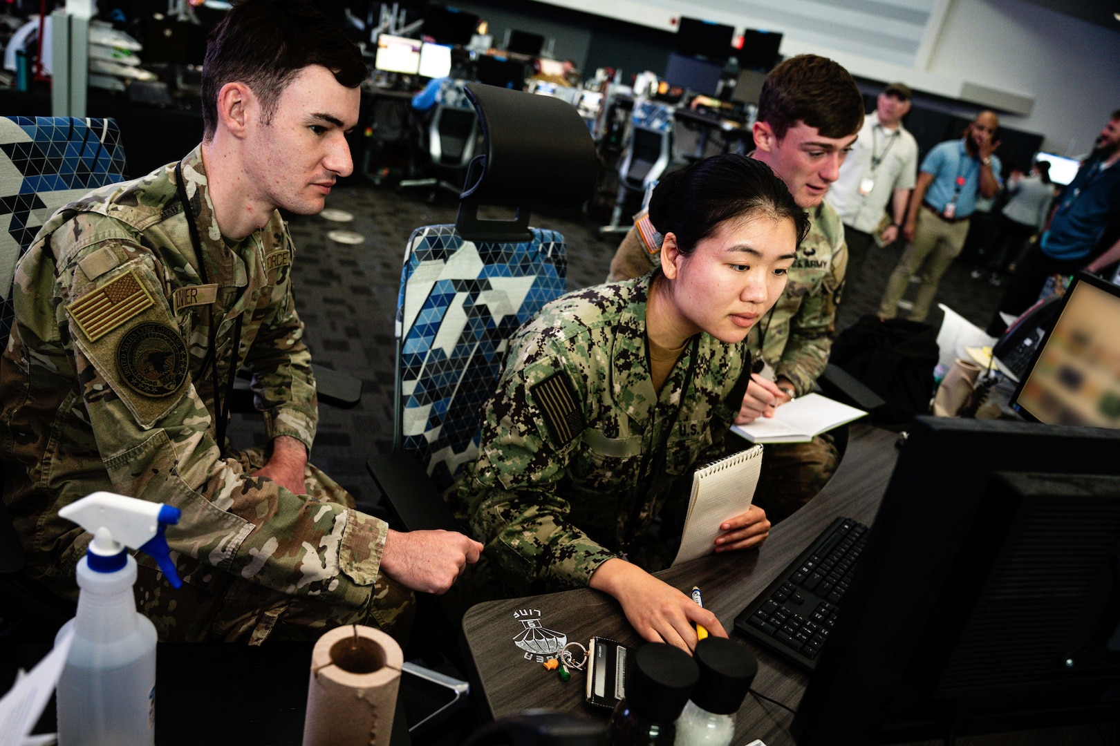 Three uniformed military personnel working at a computer