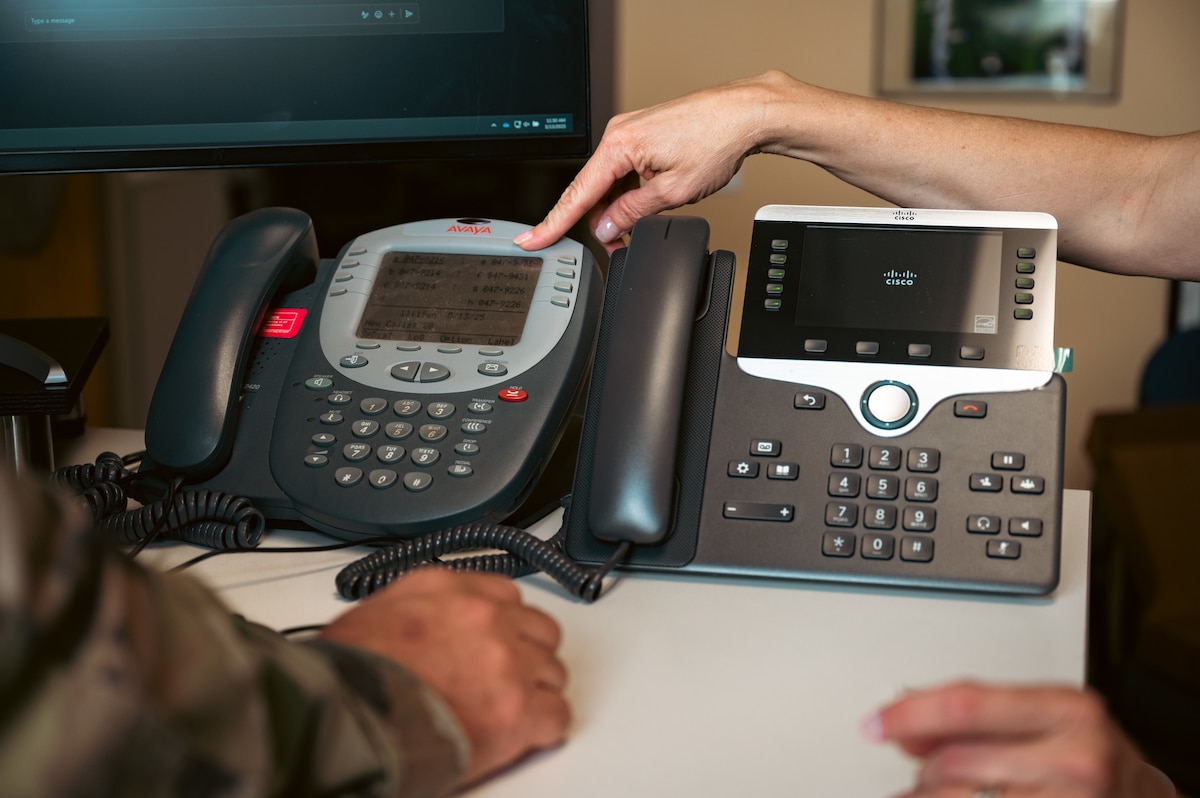 Woman points to phone on desk.