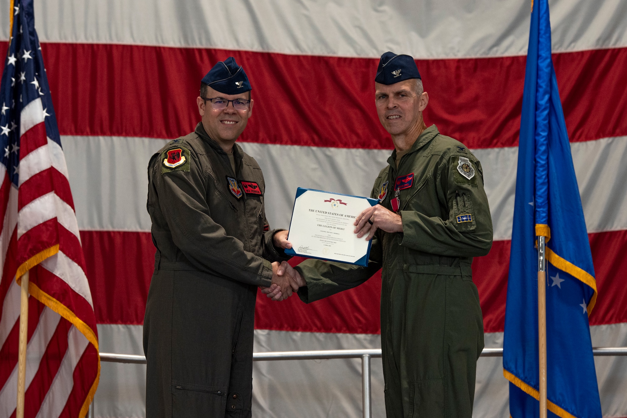 A man in a military flight suits presents a certificate to another man in a military flight suit.