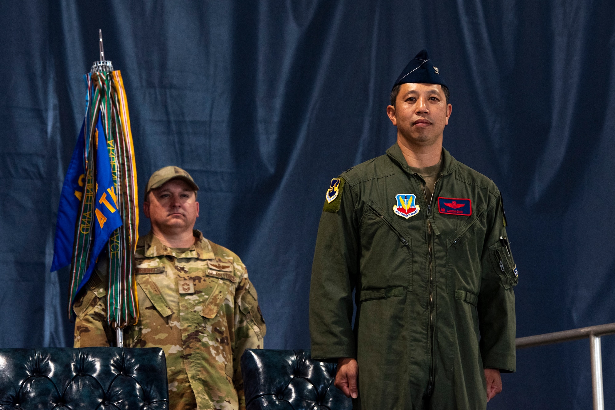 A man in a military flight suit stands at attention on a stage.