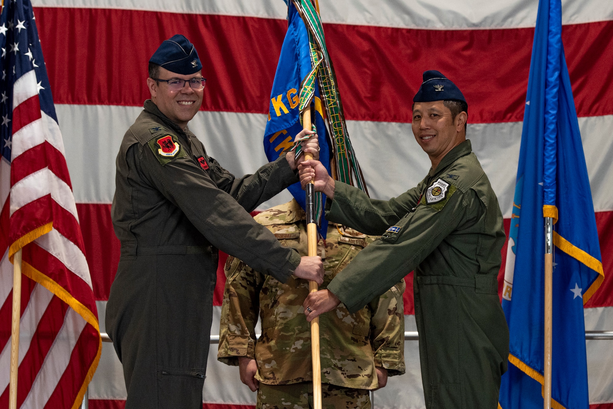 A man in a military flight suit hands a guidon to another man in a flight suit.