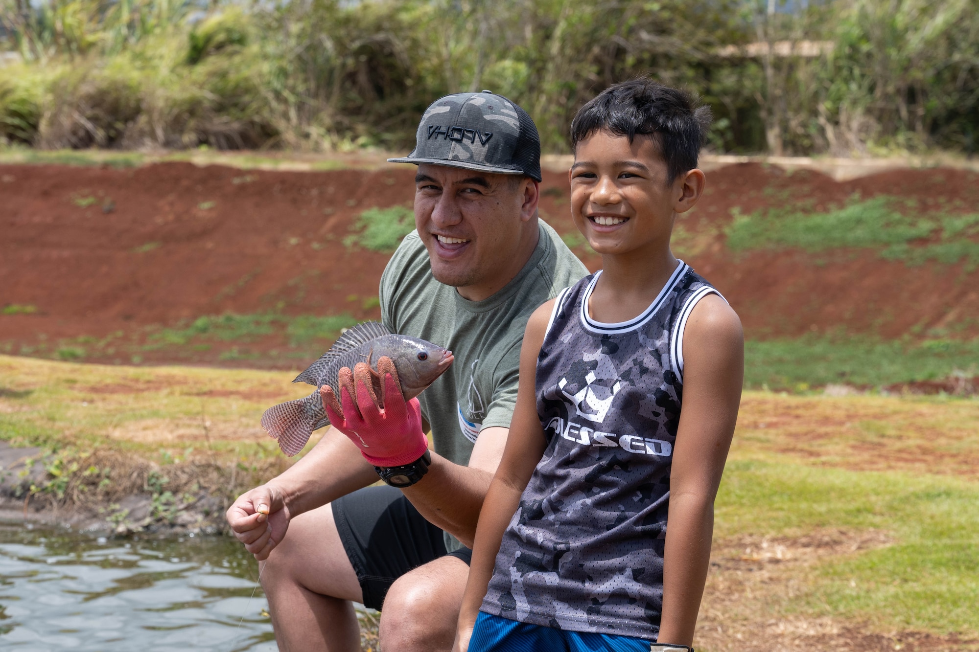 A boy and his father pose for a photo while holding a fish.