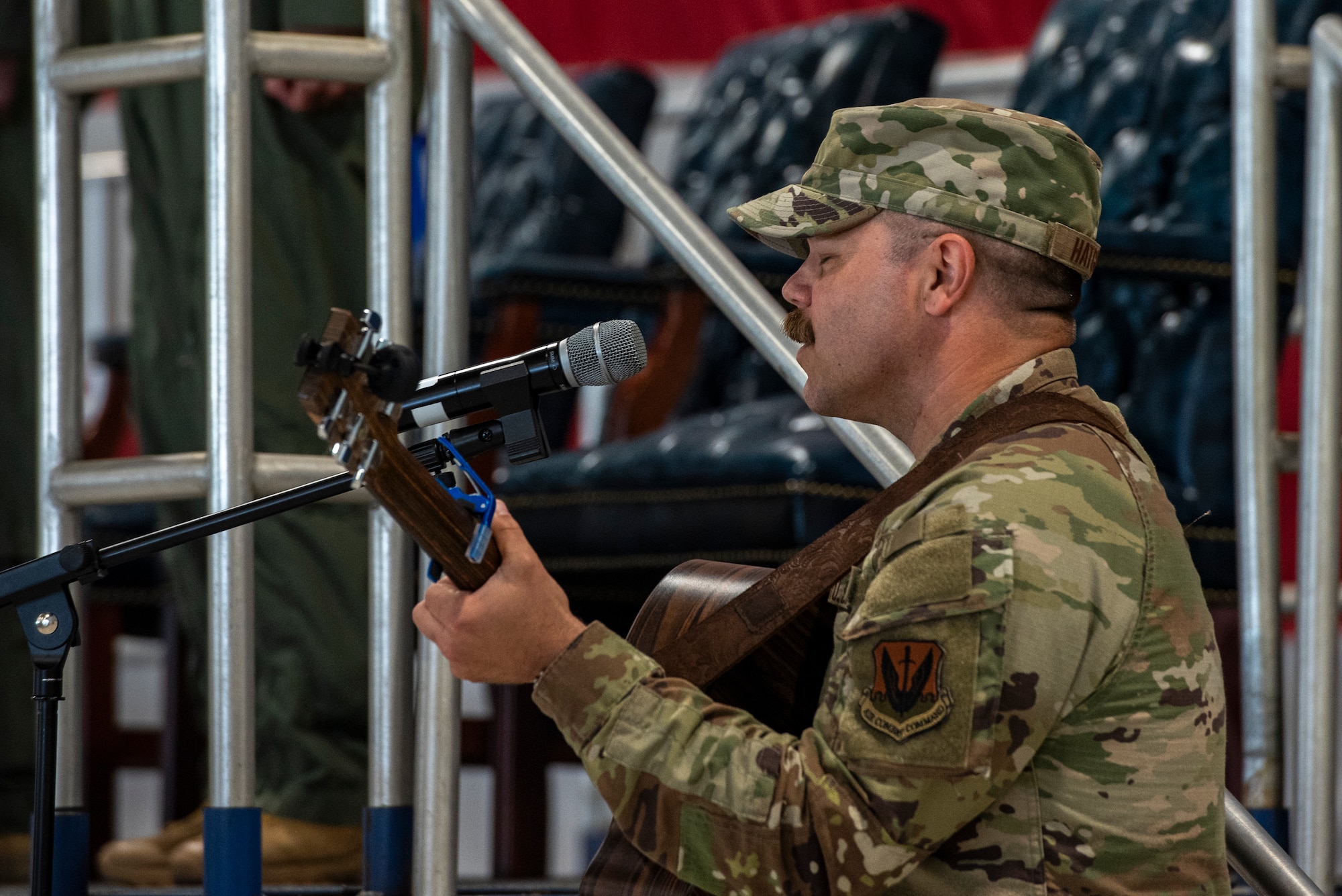 A man in a military uniform plays guitar and sings into a microphone.