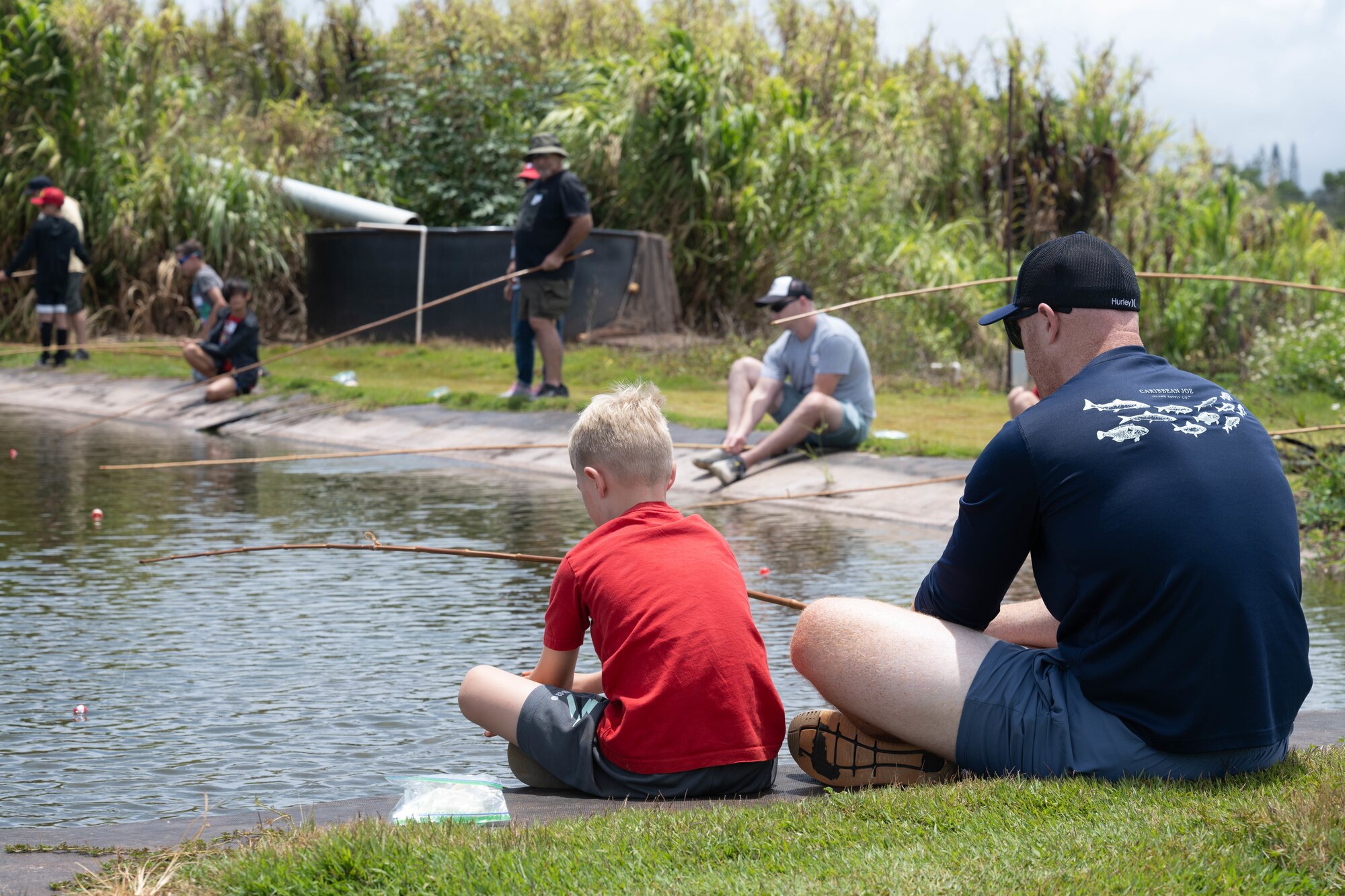 A son and his father hold fishing poles while sitting together.