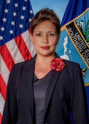 Posed photo of a woman in a dark blue suit with flags in the background.