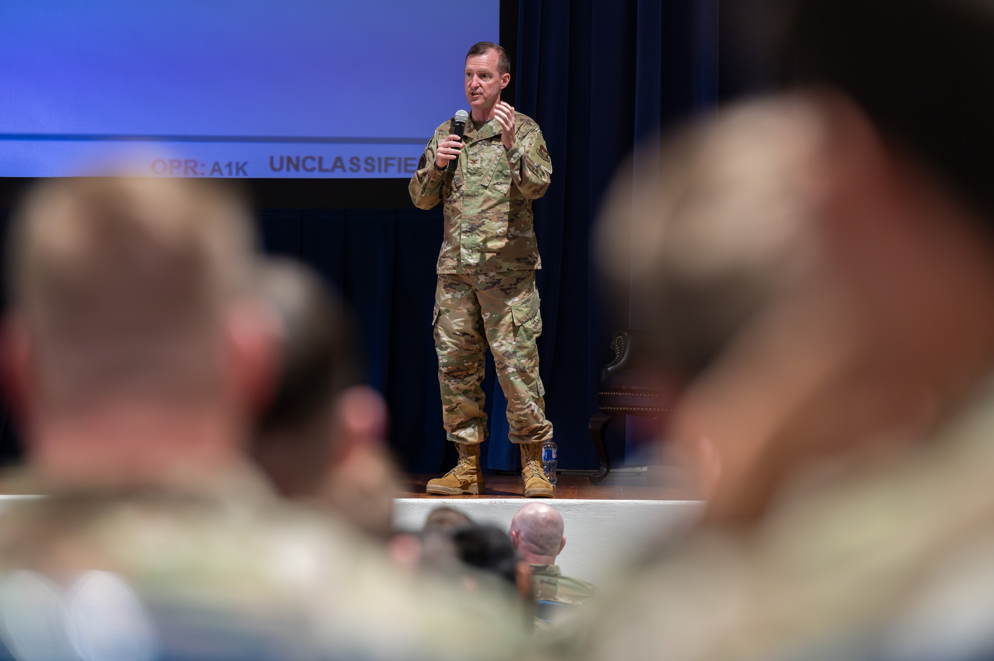 An individual in military uniform standing on a stage while addressing a crowd.