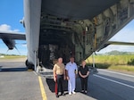 two uniformed men and one civilian woman stand at the opening of a C-130 plane