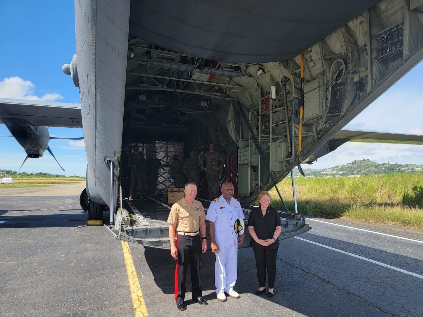 two uniformed men and one civilian woman stand at the opening of a C-130 plane