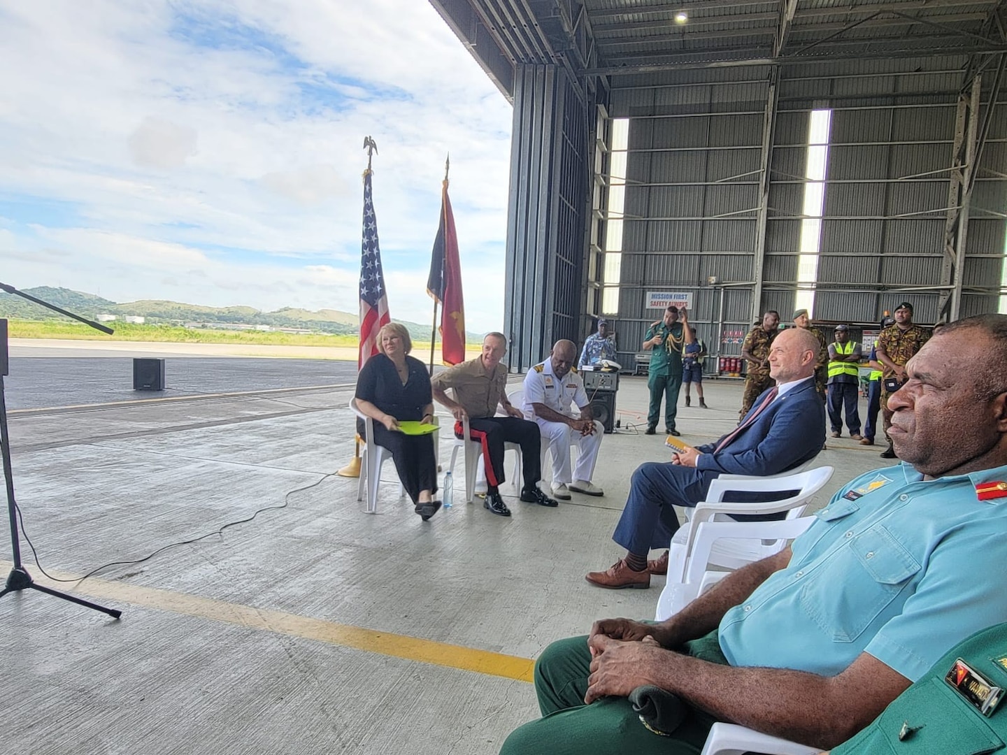 civilian and uniformed men and women site and stand near airport runway