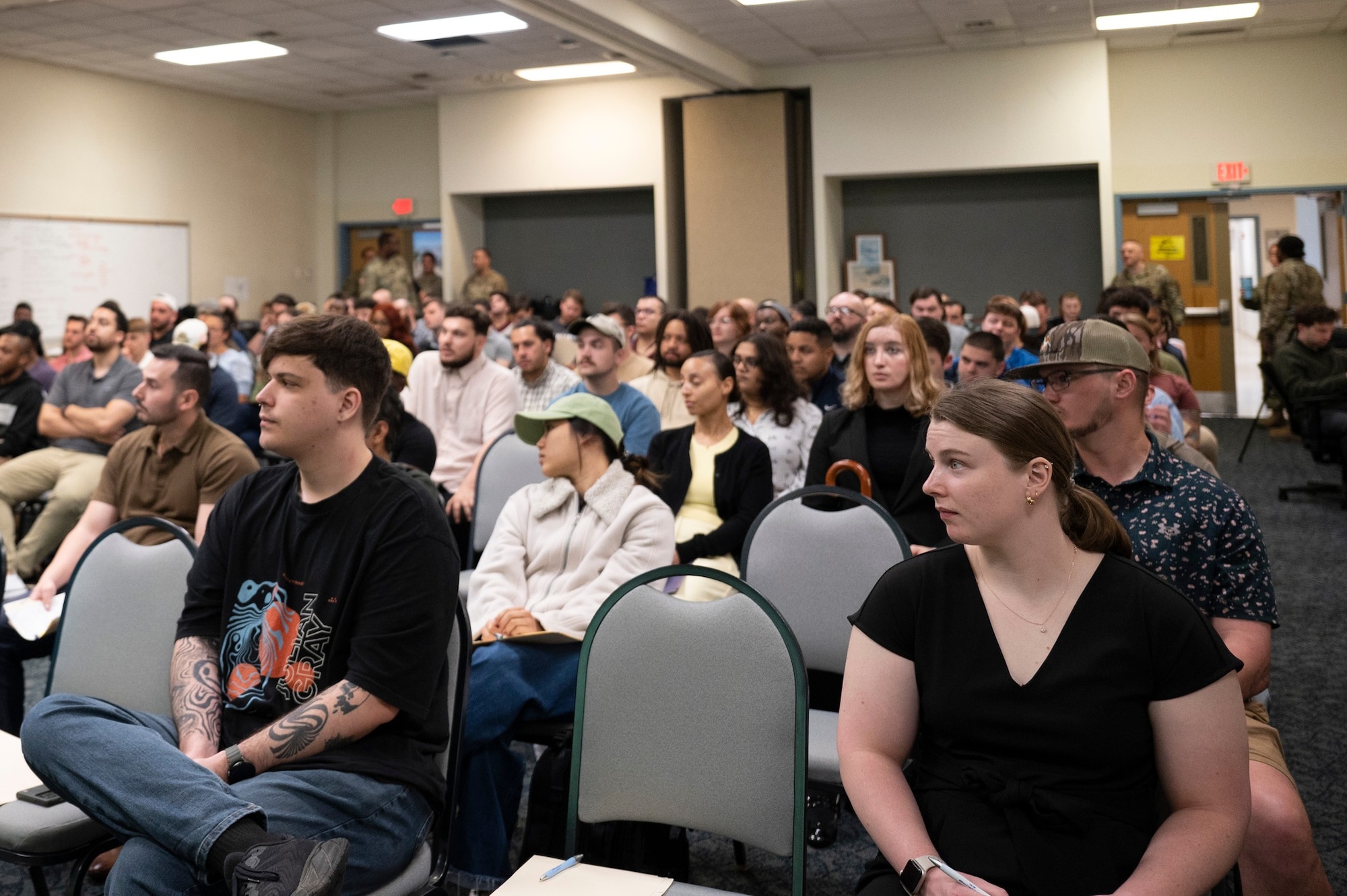 A crowd is shown seated in a crowded room with only a few empty chairs.