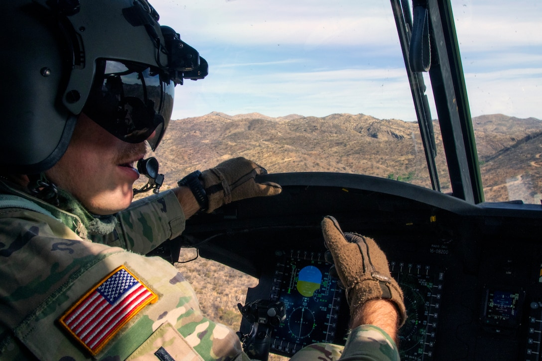A pilot speaks with someone not pictured while flying in an aircraft over a mountainous area on a sunny day.
