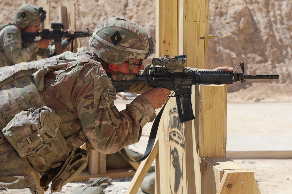 A soldier in tactical gear aims a military weapon on a wooden structure.