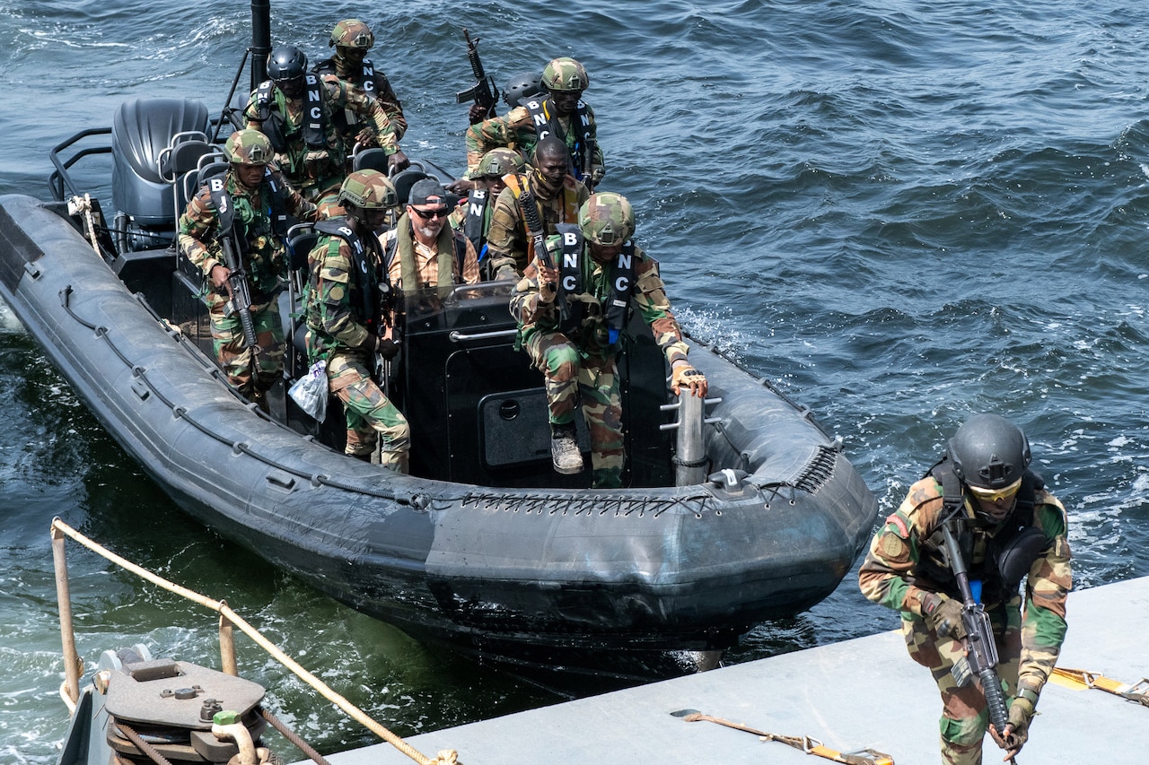 Armed men wearing camouflage military uniforms board a ship from a small boat at sea.