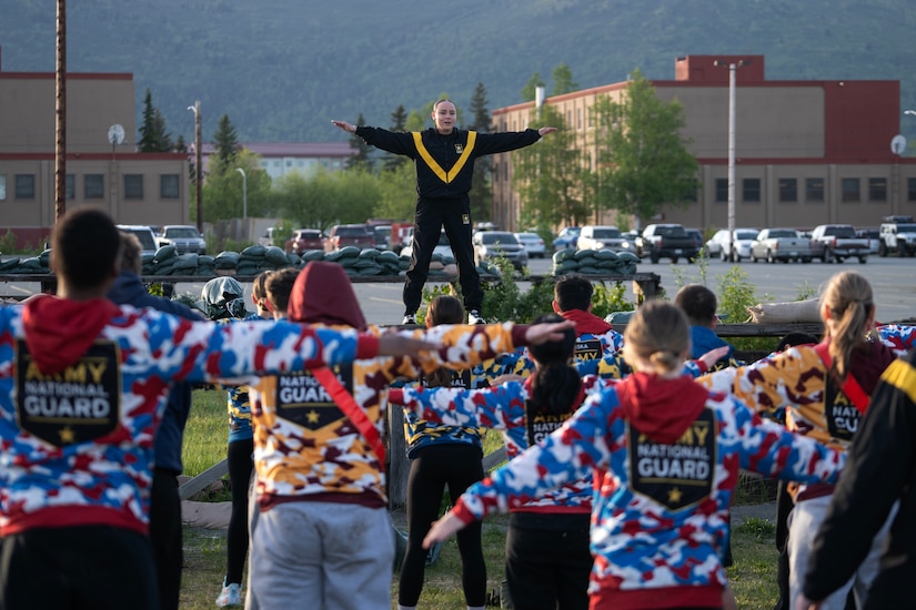 Alaska Army National Guard Spc. Katlyn Olexa, a recruiter assistant assigned to the Recruiting and Retention Battalion, leads a morning physical fitness session for Junior Reserve Officer Training Corps cadets from Dimond, Bartlett, Service, East, Colony and the Bethel Regional high schools at Joint Base Elmendorf-Richardson, Alaska, May 29, 2025. The PT session was part of the JROTC Cadet Leadership Challenge camp, designed to develop leadership skills, teamwork, and military discipline among the cadets. Alaska Army National Guard Recruiting and Retention Battalion personnel served as safety observers and mentors, providing guidance, and sharing their expertise to enhance the cadets’ training experience.