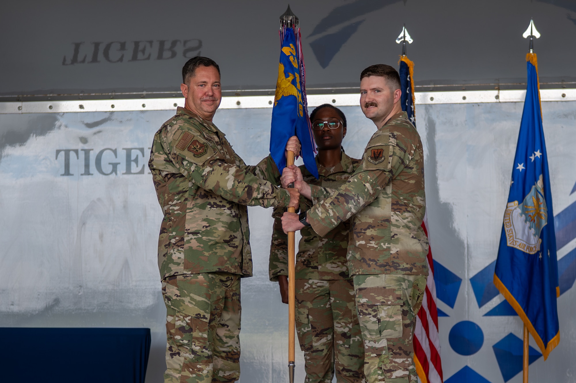 Man in uniform passes a guidon to another man in uniform.