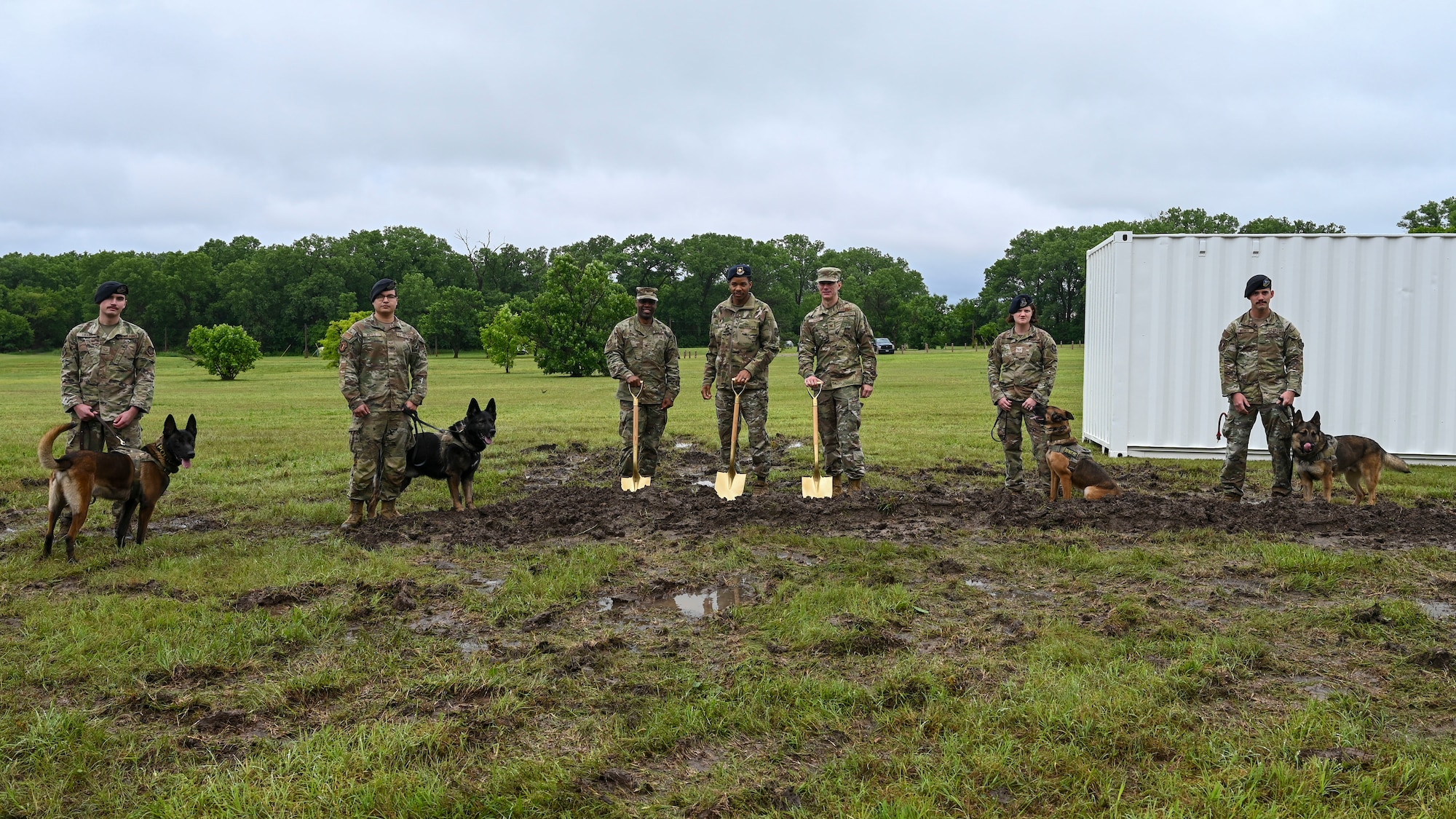 People in military uniforms pose with golden shovels and military working dogs.