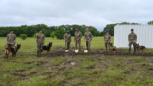 People in military uniforms pose with golden shovels and military working dogs.