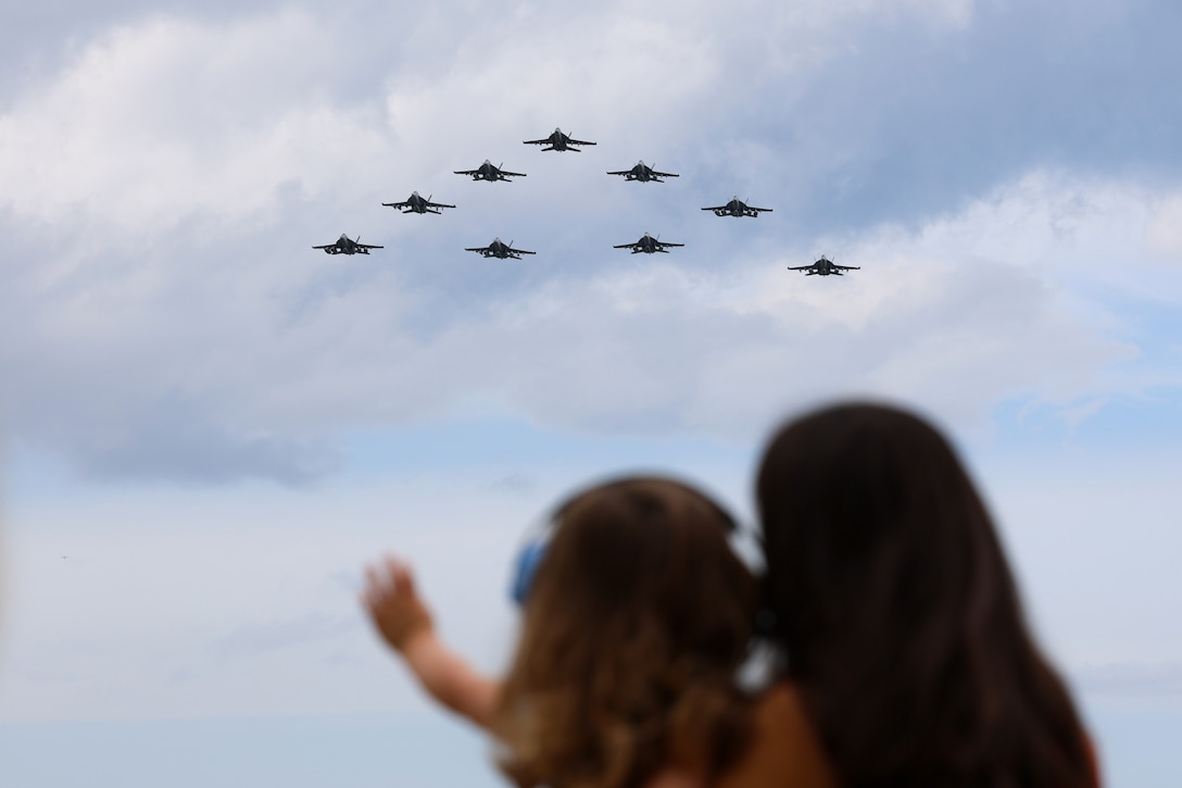 A group of Navy aircraft fly in formation while a child points and a person watches.