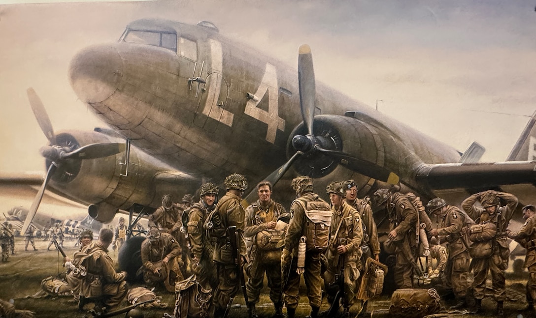 A military painting displaying men standing and sitting in uniform and carrying parachutes in front of a plane.