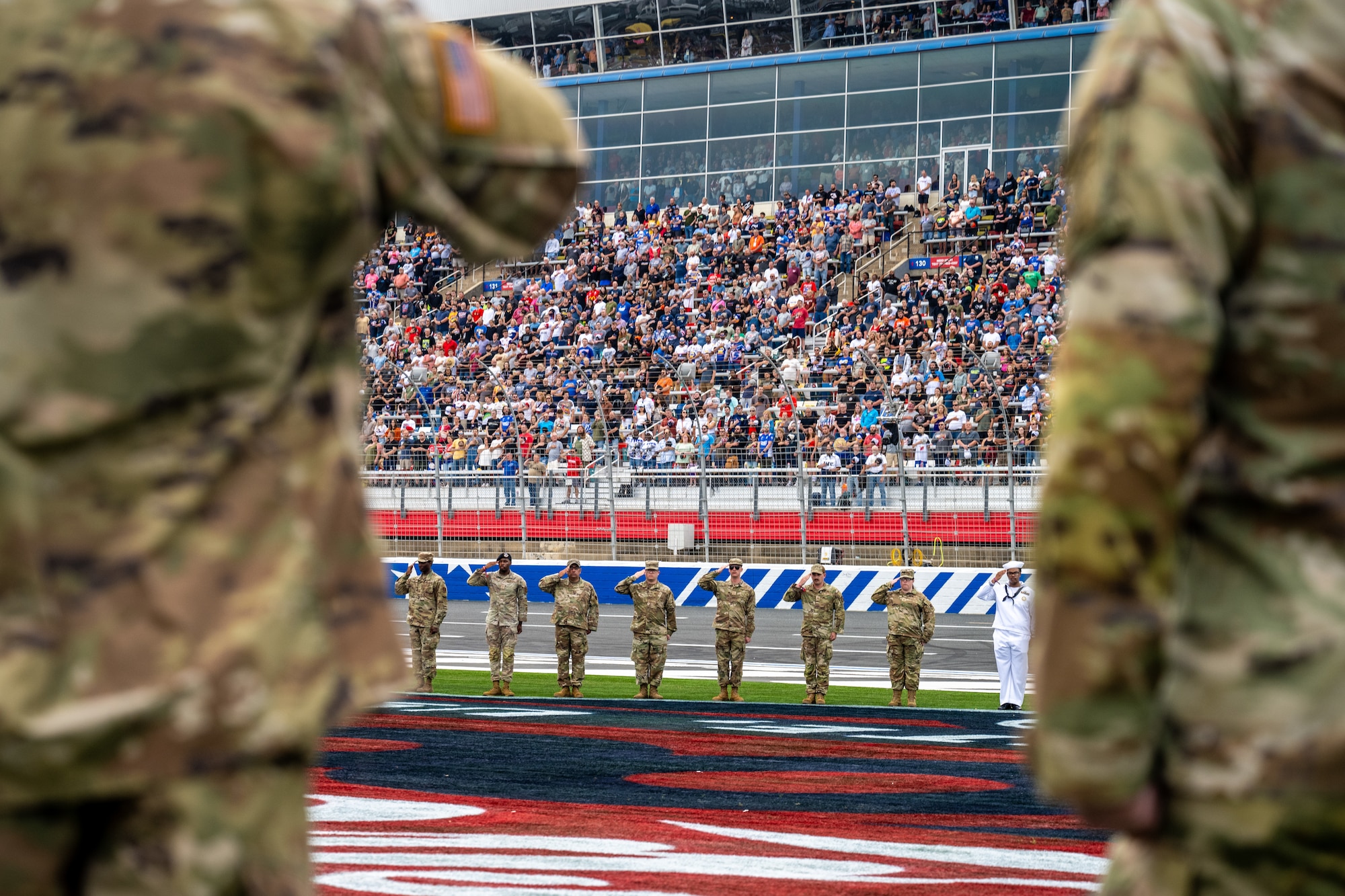 Joint service members render military salutes during a pre-race memorial while B-2 Spirit stealth bombers formation