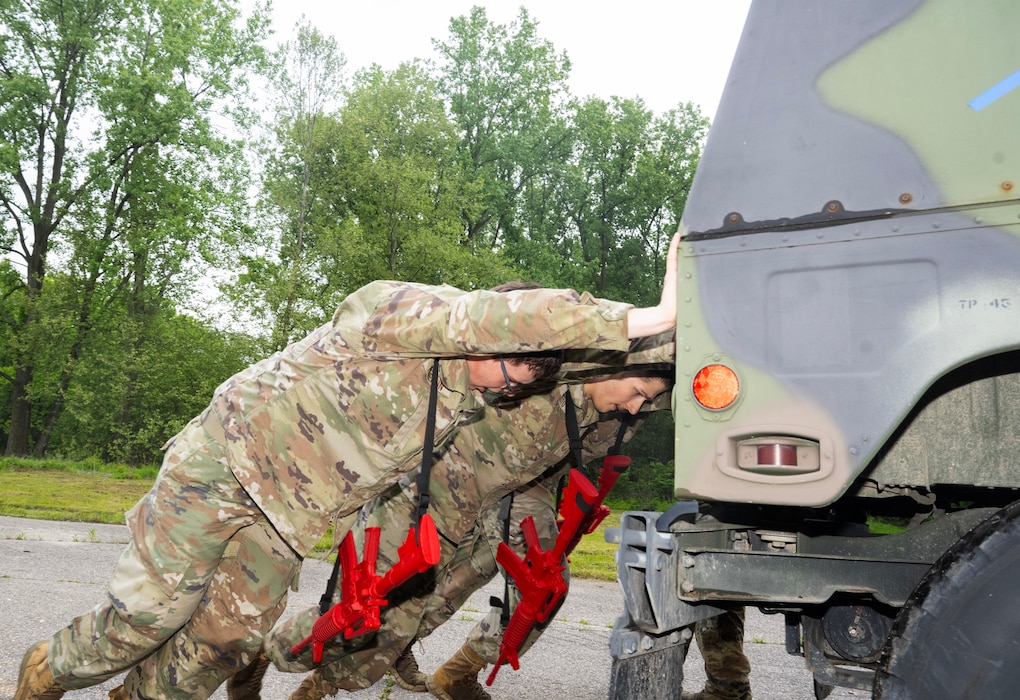 A line of Airmen push with all their strength against the back of a Humvee.