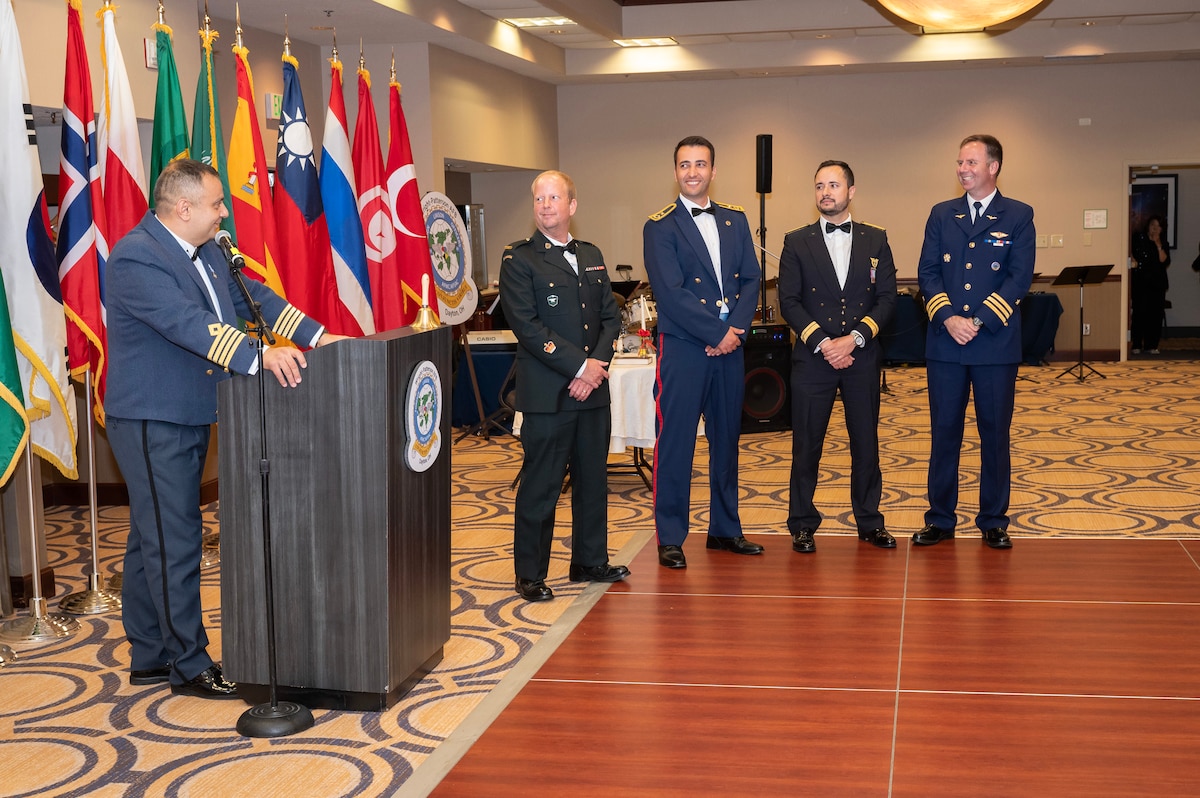 5 men in formal attire stand in front of ballroom.