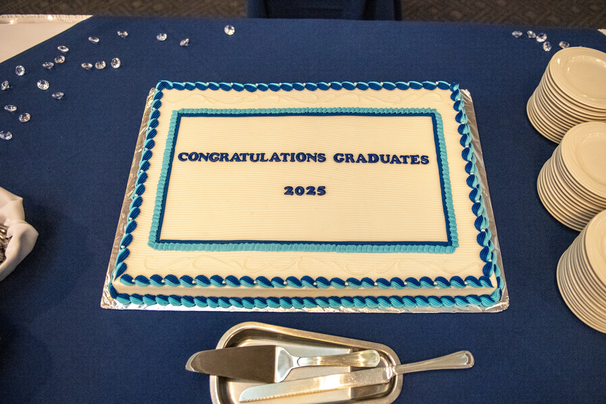 A cake, topped with white, dark blue and light blue icing, for the graduating CCAF class is displayed on a table with silverware sitting below.
