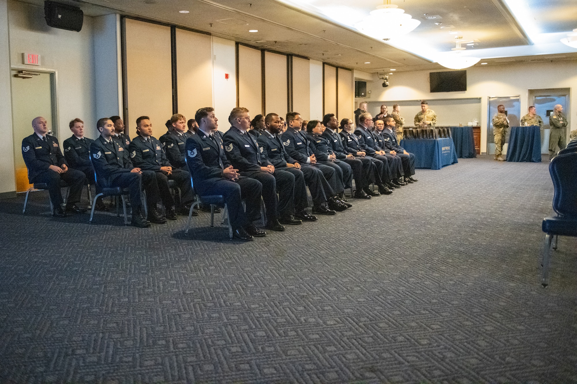 A group of U.S. Airmen dressed in their blue service dress, sit in chairs.