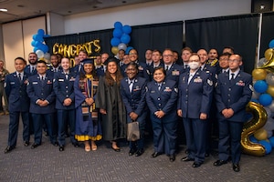A group of U.S. Air Force Airmen and others pose for a photo in front of balloons at a graduation ceremony.