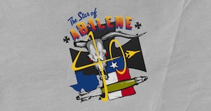 A longhorn skull sits above a vertical Texas flag and beside a silhouette of the state, referencing elements found in past B-1 nose art. Below the design is a Joint Direct Attack Munition bomb, representative of the B-1’s payload. “The Star of Abilene” appears above, referencing the first B-1 delivered to Dyess AFB. The red, white, blue, grey, and yellow color palette reflects the Texas flag, the aircraft’s metal, and the 7th Bomb Wing crest. Three black crosses in the background symbolize the 7th BW.
