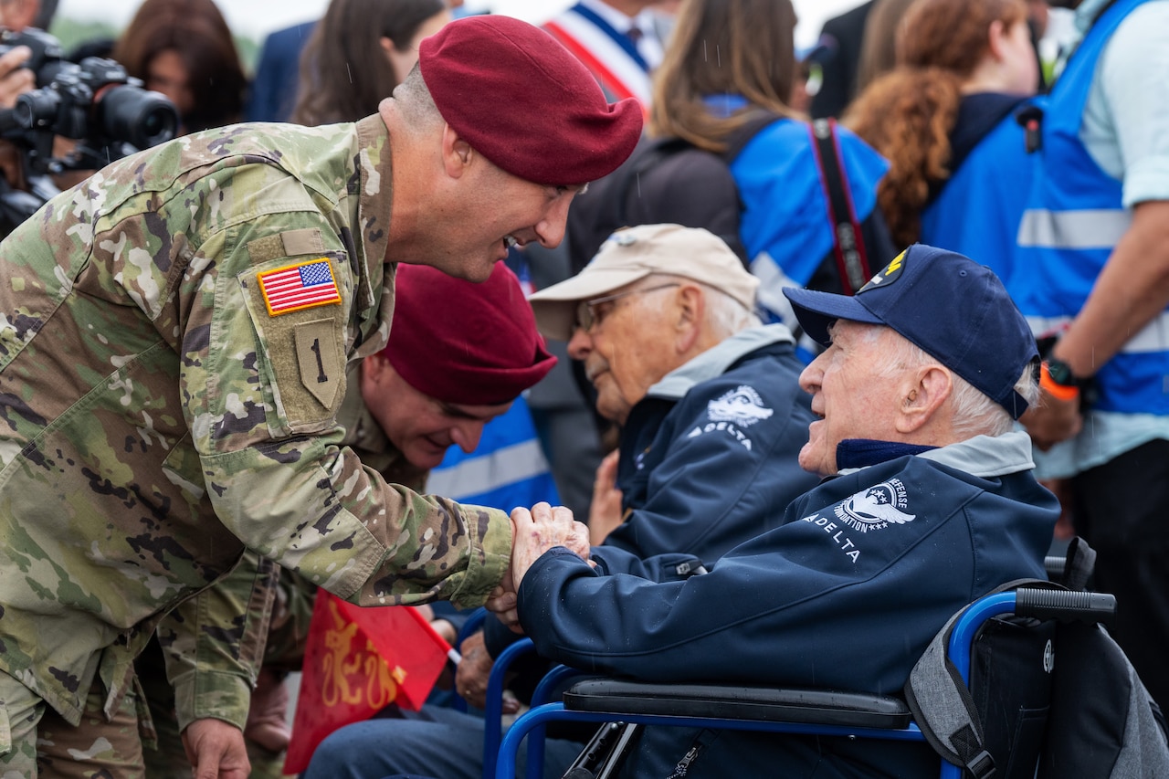 A soldier greets a veteran sitting on a wheelchair surrounded by people