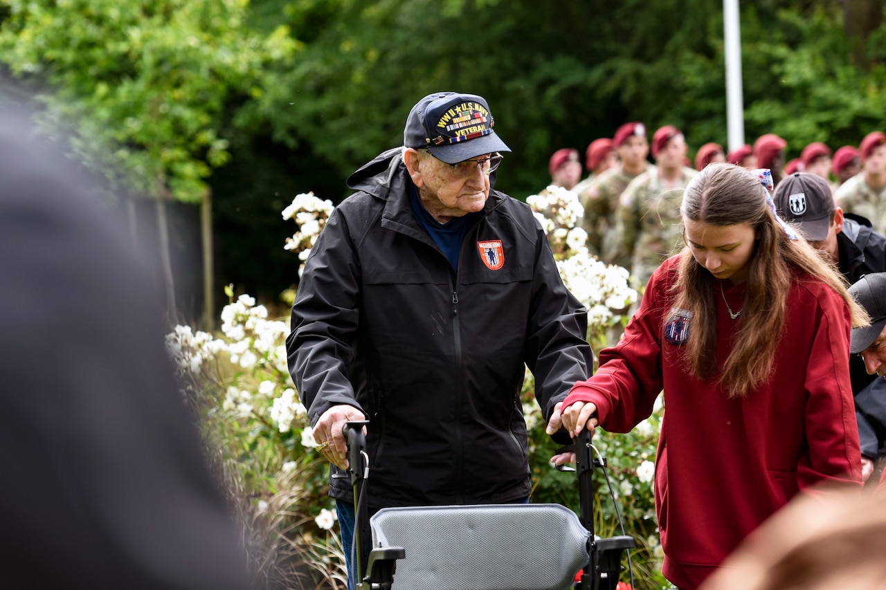 A veteran walks with a walker while assisted by a woman.