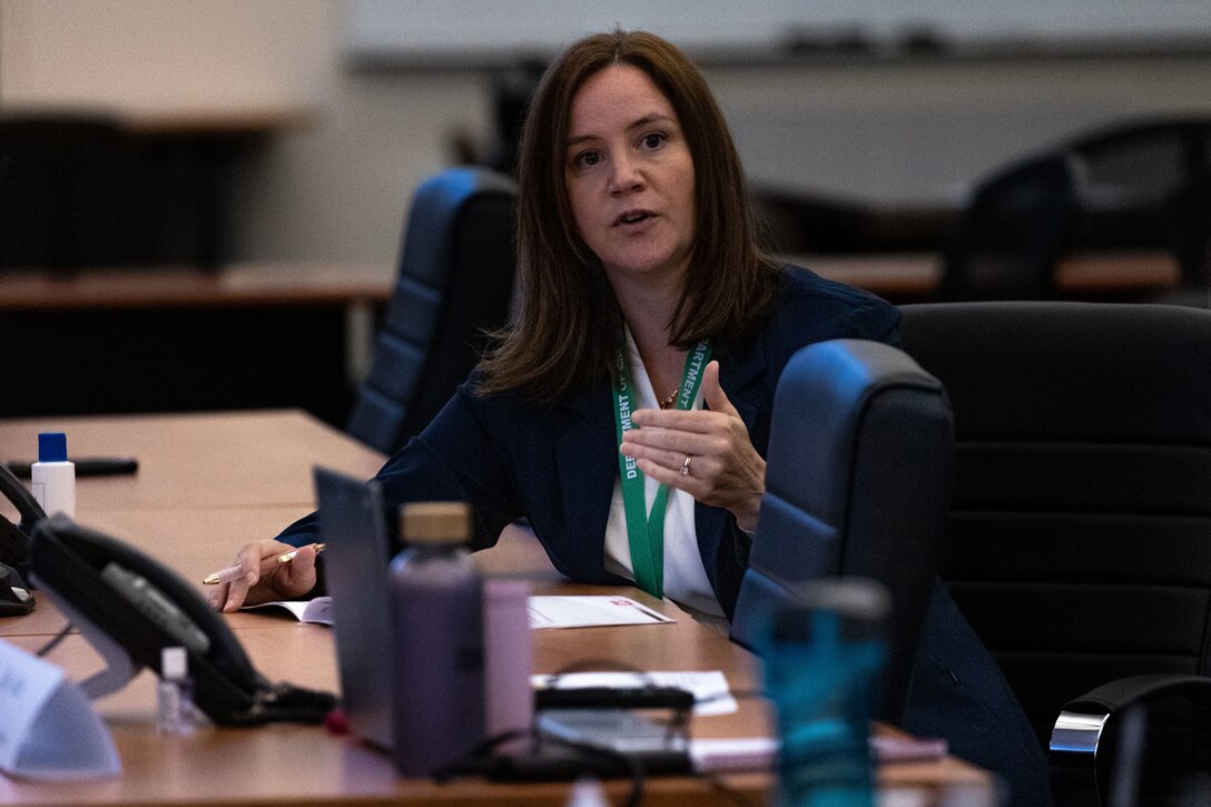 A woman speaks to an audience while sitting at a table.