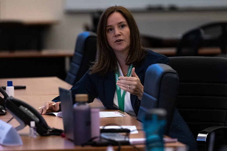 A woman speaks to an audience while sitting at a table.