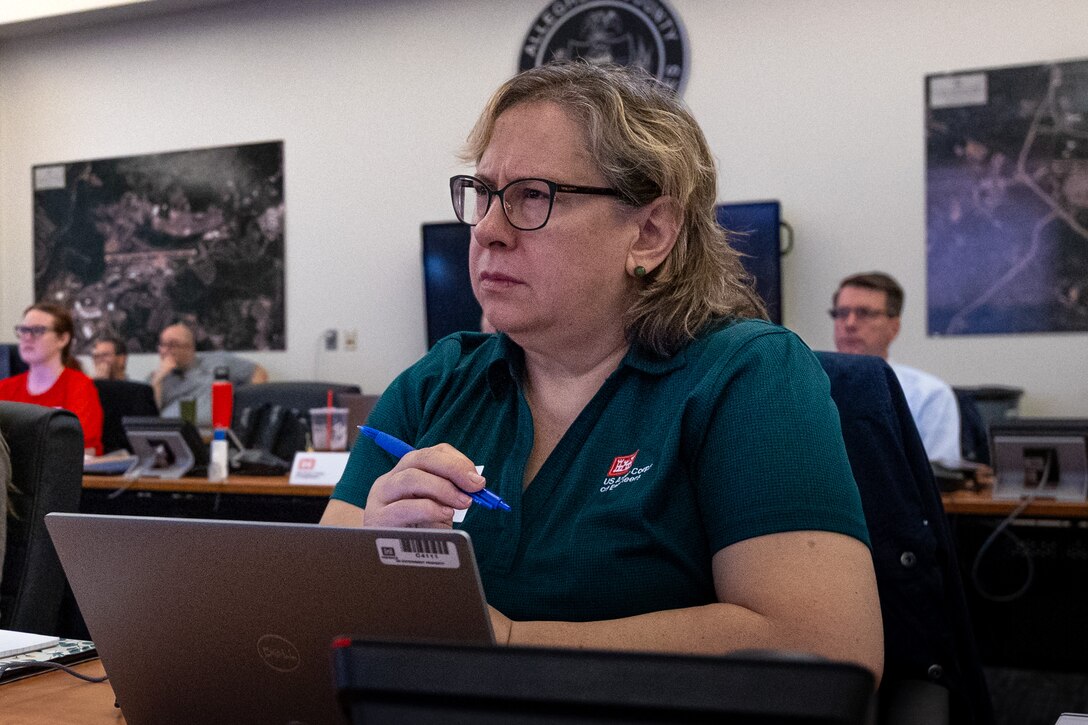 A woman sits at a table watching a presentation.