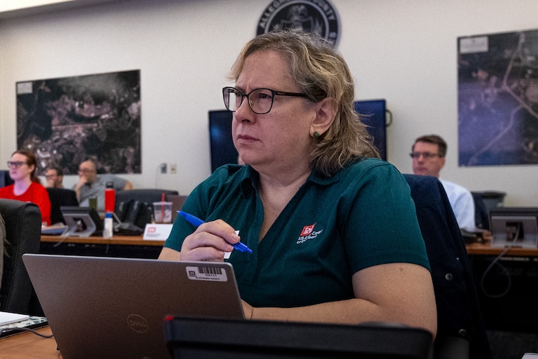 A woman sits at a table watching a presentation.