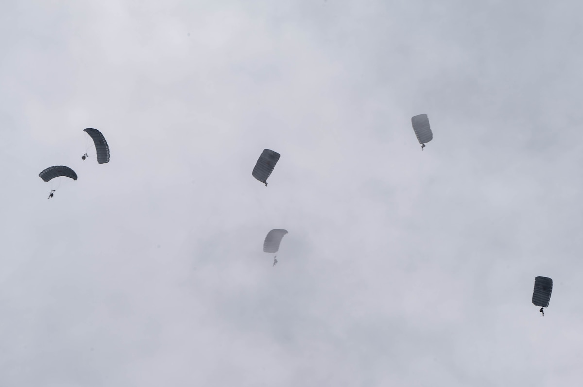 Pararescue specialists steer their parachutes toward the drop zone