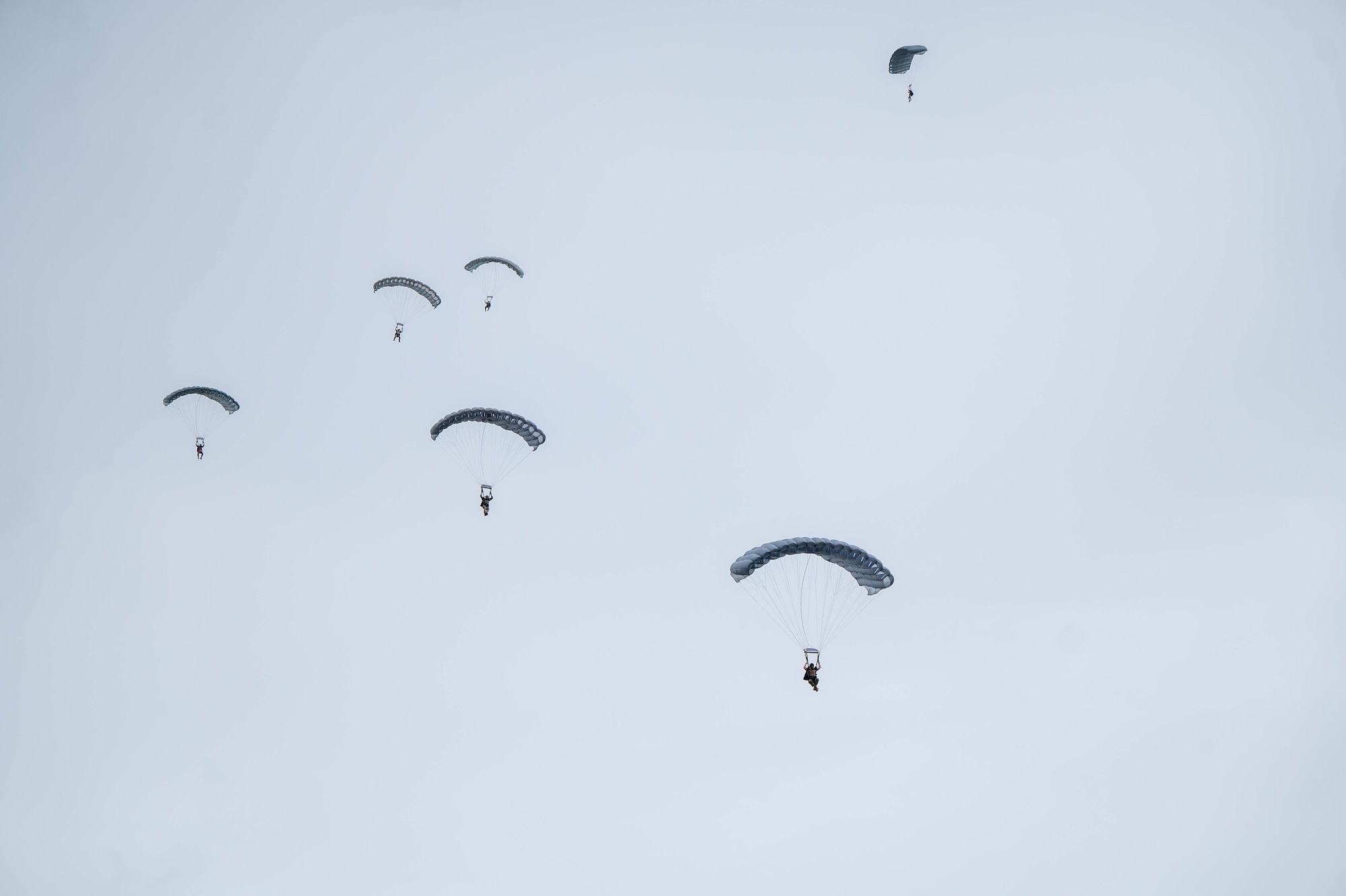 Pararescue specialists descend in a stack formation toward the drop zone